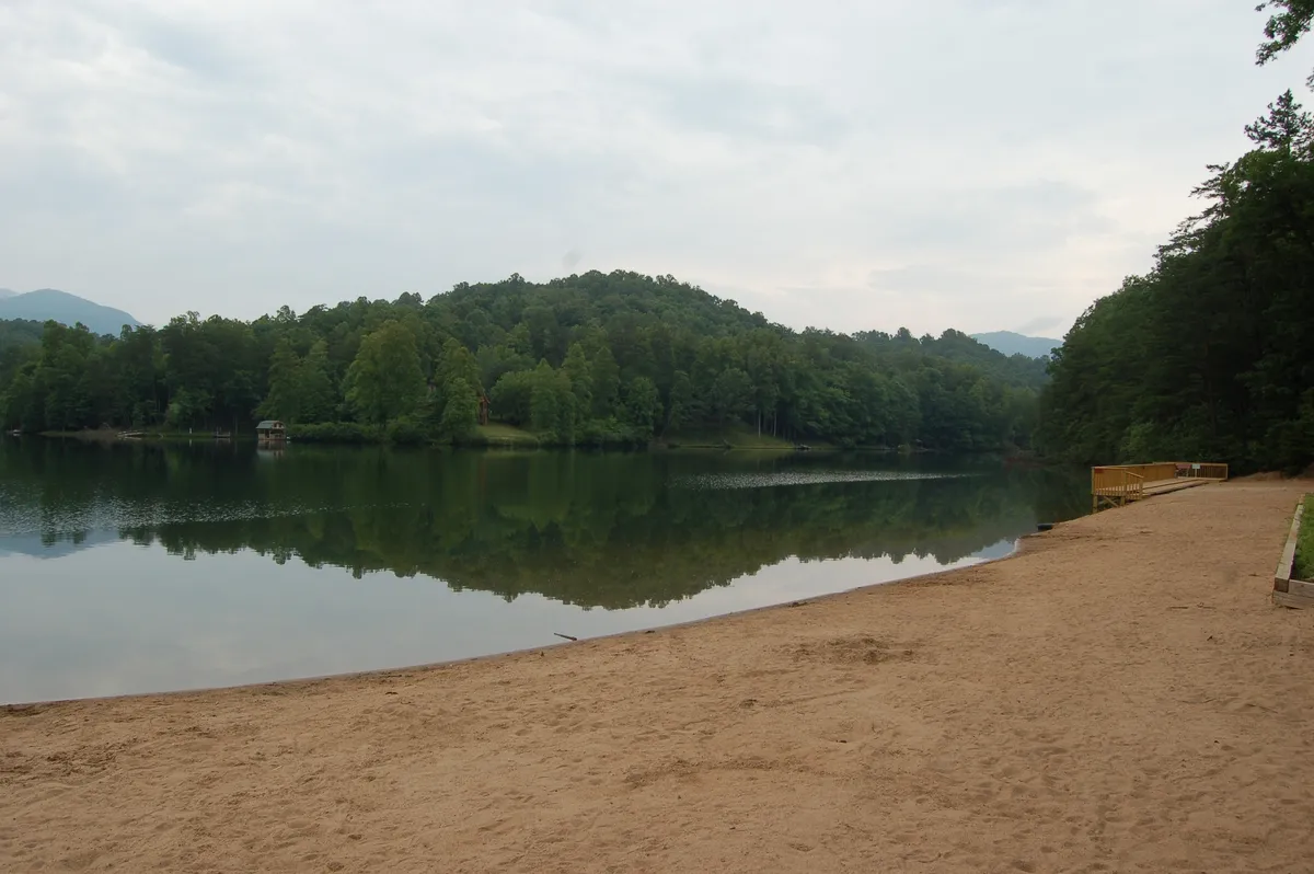A wide view of a calm lake bordered by greenery and a sandy beach, inviting visitors to swim, picnic, fish, or simply unwind by the water. The tranquil atmosphere and natural beauty capture the essence of a private outdoor escape.