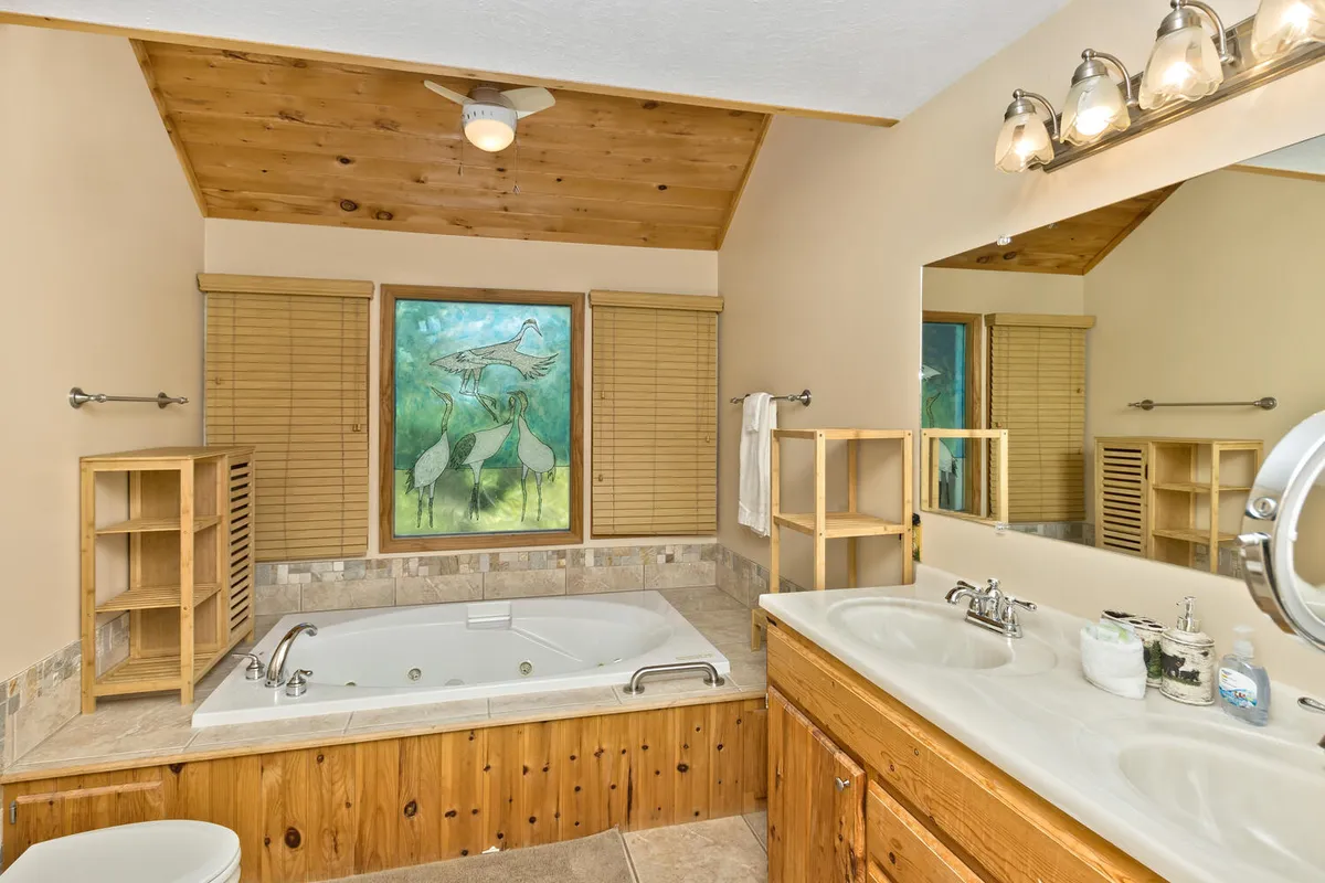 A serene bathroom centered around a luxurious jacuzzi tub, accompanied by framed nature artwork and wooden shelving. The ambiance is spa-like, inviting guests to unwind and enjoy a calming soak after a day of adventure.