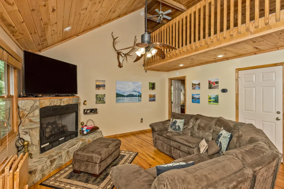 The image showcases a spacious, open living area with a large sectional sofa arranged around a stone fireplace. Mounted antlers and tasteful artwork adorn the walls, adding a rustic yet refined touch. The warm glow from the fire and the inviting seating arrangement convey a welcoming atmosphere ideal for group gatherings or quiet relaxation.