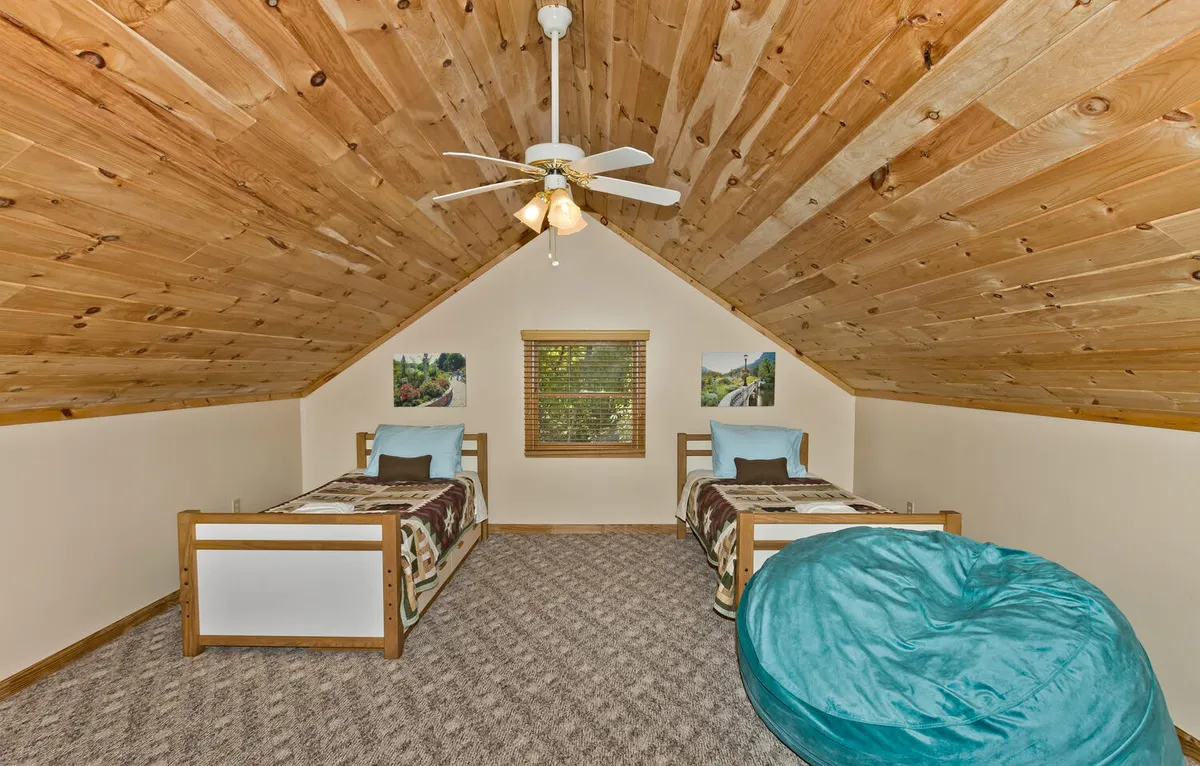 A playful and comfortable bedroom setup with two twin beds, a large bean bag chair, and a wooden ceiling. The space is inviting for reading, playing games, or relaxing, perfect for both kids and adults seeking a private sanctuary.