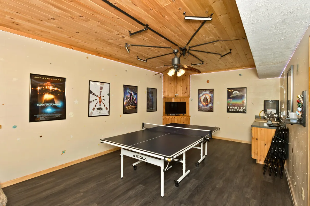 This image features a lively game room setup, complete with a ping pong table, movie posters on the walls, and a TV setup in the background. The atmosphere is playful, energetic, and designed for group fun, inviting friendly competition and movie nights alike.