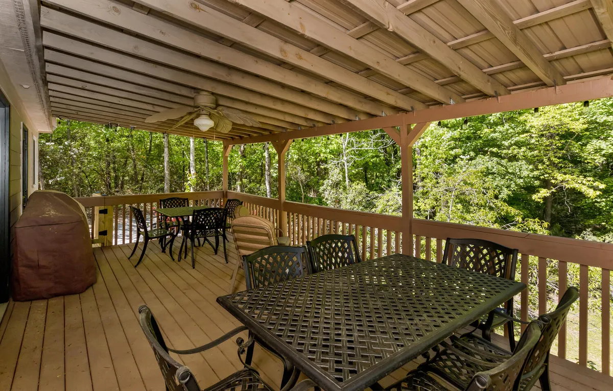 This image captures an inviting outdoor patio area with a metal table and black wrought iron chairs, framed by a sturdy wooden railing and lush green foliage in the background. The setting suggests a secure, welcoming space where guests can relax, dine, or socialize under the open sky.