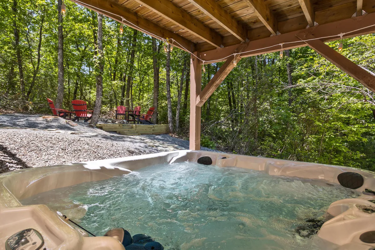 A scenic outdoor deck overlooks the surrounding trees, furnished with Adirondack chairs and a hot tub. The tranquil mood invites guests to enjoy their morning coffee or unwind while taking in the forest views, seamlessly blending comfort with natural beauty.