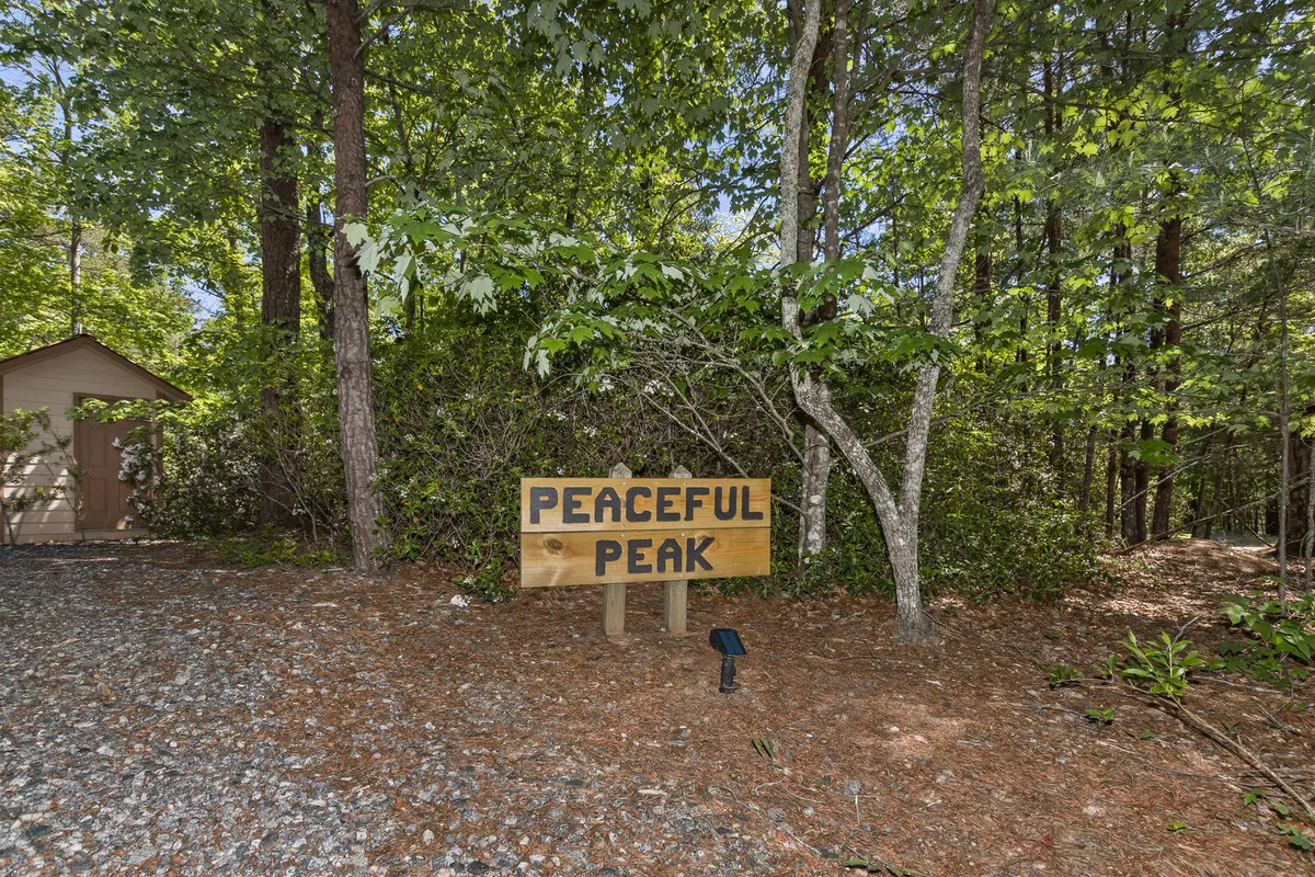A serene outdoor scene showing a wooden signpost, gravel path, and surrounding woods. The gravel road is sheltered by tall trees, offering a peaceful track ideal for pet walks and nature exploration. The setting feels private and secure, inviting strolls right from the cabin door.