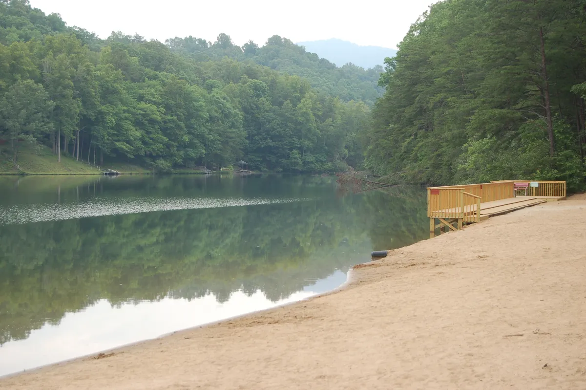 A calm, community lake bordered by trees, featuring a wooden dock jutting out into the water. The stillness of the lake and the natural surroundings invite swimming, fishing, picnicking, and other non-motorized activities exclusively for community guests.