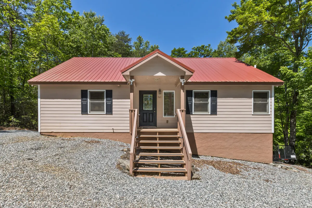 An exterior shot showcasing the front porch with a red metal roof, a stone pathway leading up to the house, and lush greenery surrounding the property. The inviting porch offers ample space for morning coffee, sunset views, or gathering with family before heading out to explore.