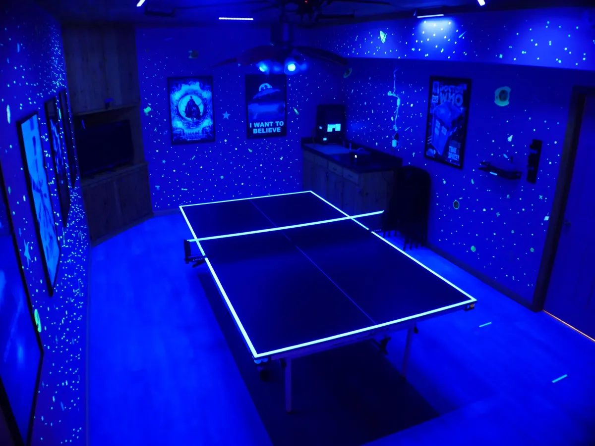 A vibrant basement scene with a glow-in-the-dark ping pong table, neon lighting, and playful wall art. The energetic space is set up for family game nights, tournaments, and social gatherings, embodying fun and togetherness regardless of the weather.