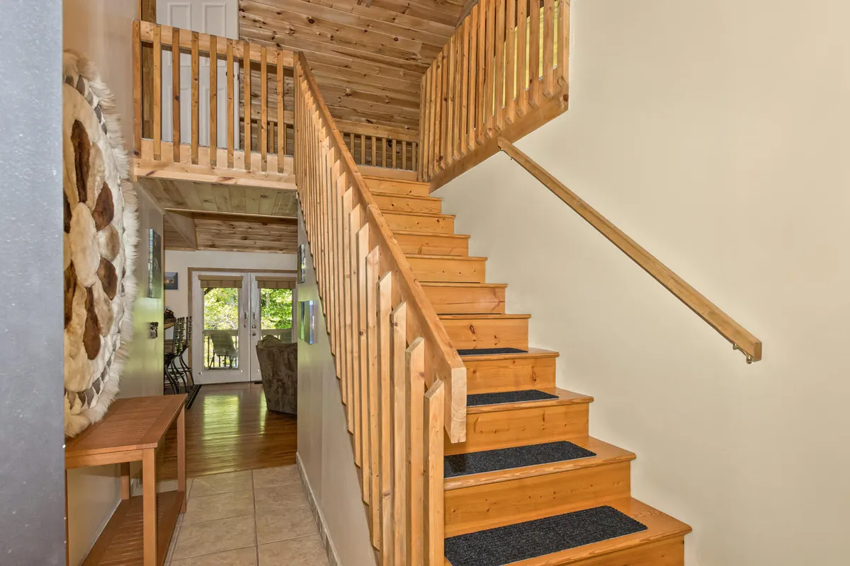 An inviting interior entryway scene, showcasing a wooden staircase, railing, and decorative wall art. The warm lighting and clean lines create an immediate sense of welcome and order as guests enter or exit the home.